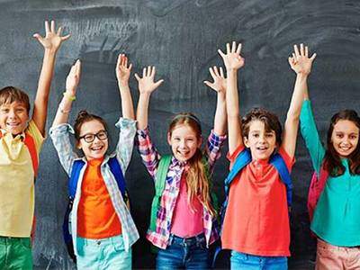 Excited children holding both hands in the air in front of a chalkboard.