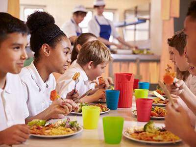 Children eating lunch and talking inn a school cafeteria.